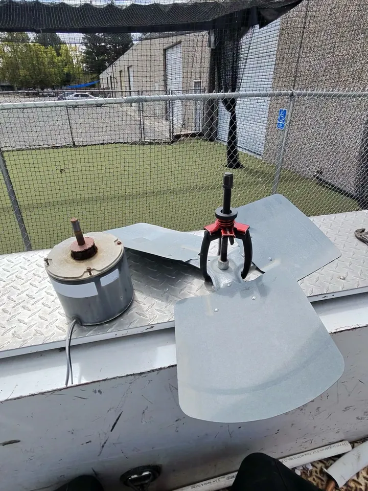 Removed condenser fan motor beside the fan blade with a puller attached to the blade hub
